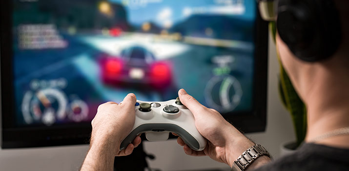 Young man holding video game controller in front of TV showing racing game.