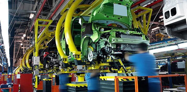 Workers in a factory place parts on partially assembled automobiles.