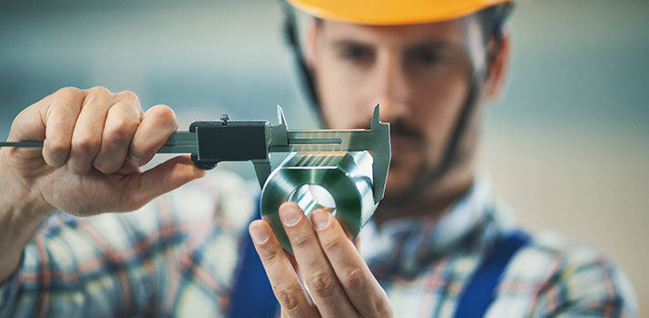 Male worker in a hardhat uses a precision tool to measure a metal cylinder.