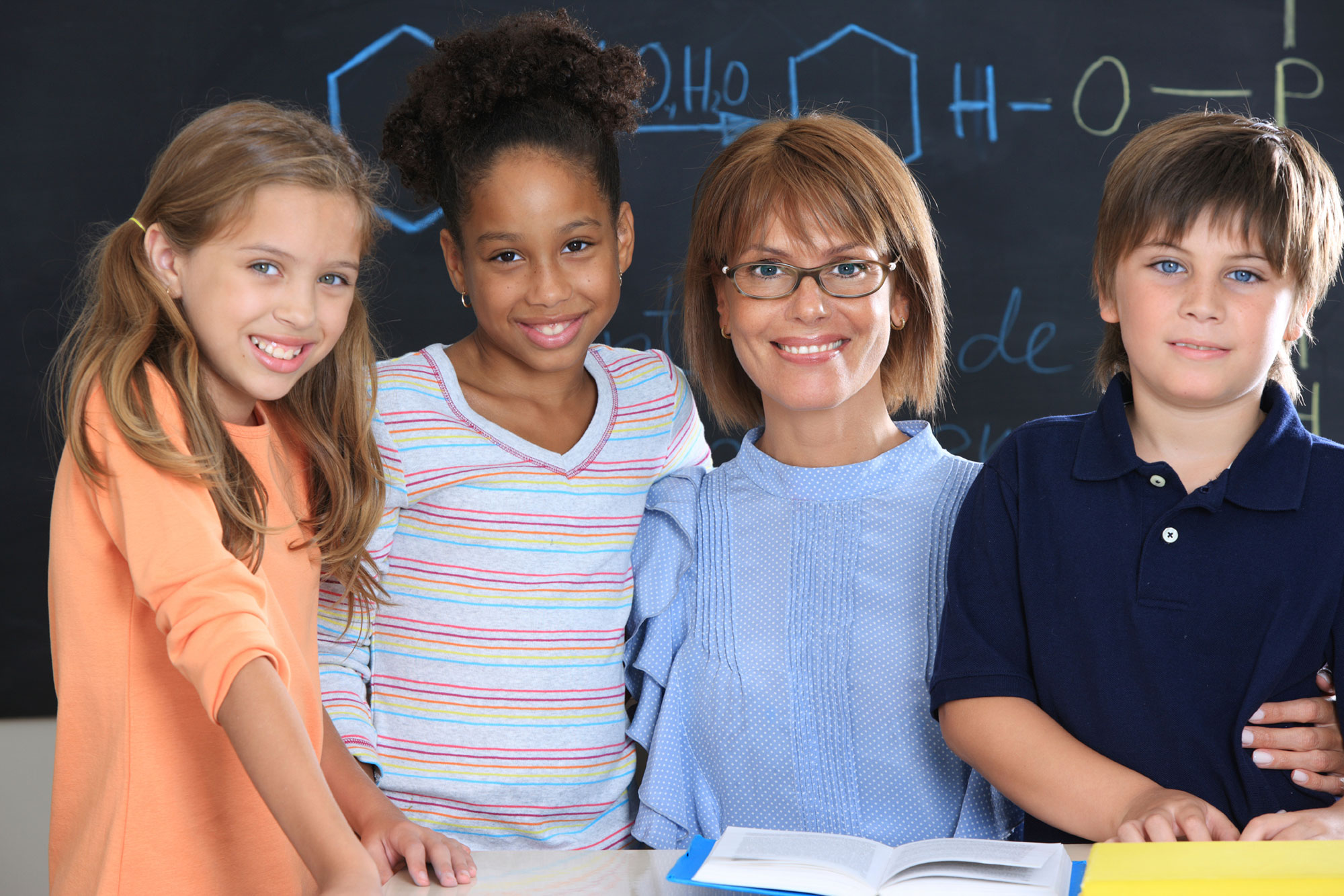 Reading teacher with three elementary school students and open books.